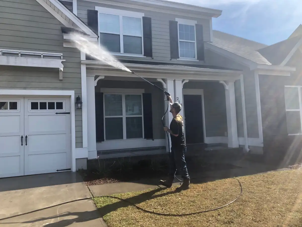 A technician reaching upper-storey siding with a soft-wash extension wand at low pressure